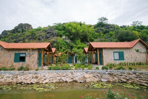 A stone building with a tiled roof, a stone wall, and a pond with lily pads. - Laco green Trang An (Hoa Lu)