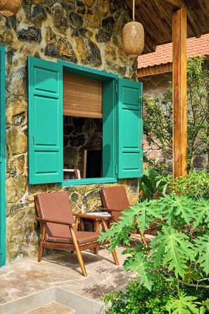 A stone building with a wooden porch, two wooden chairs, and a wicker hanging light fixture. - Laco green Trang An (Tay Hoa Lu)
