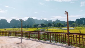 A wooden deck with a railing overlooking a rice field and mountains. - Laco green Trang An (Tay Hoa Lu)