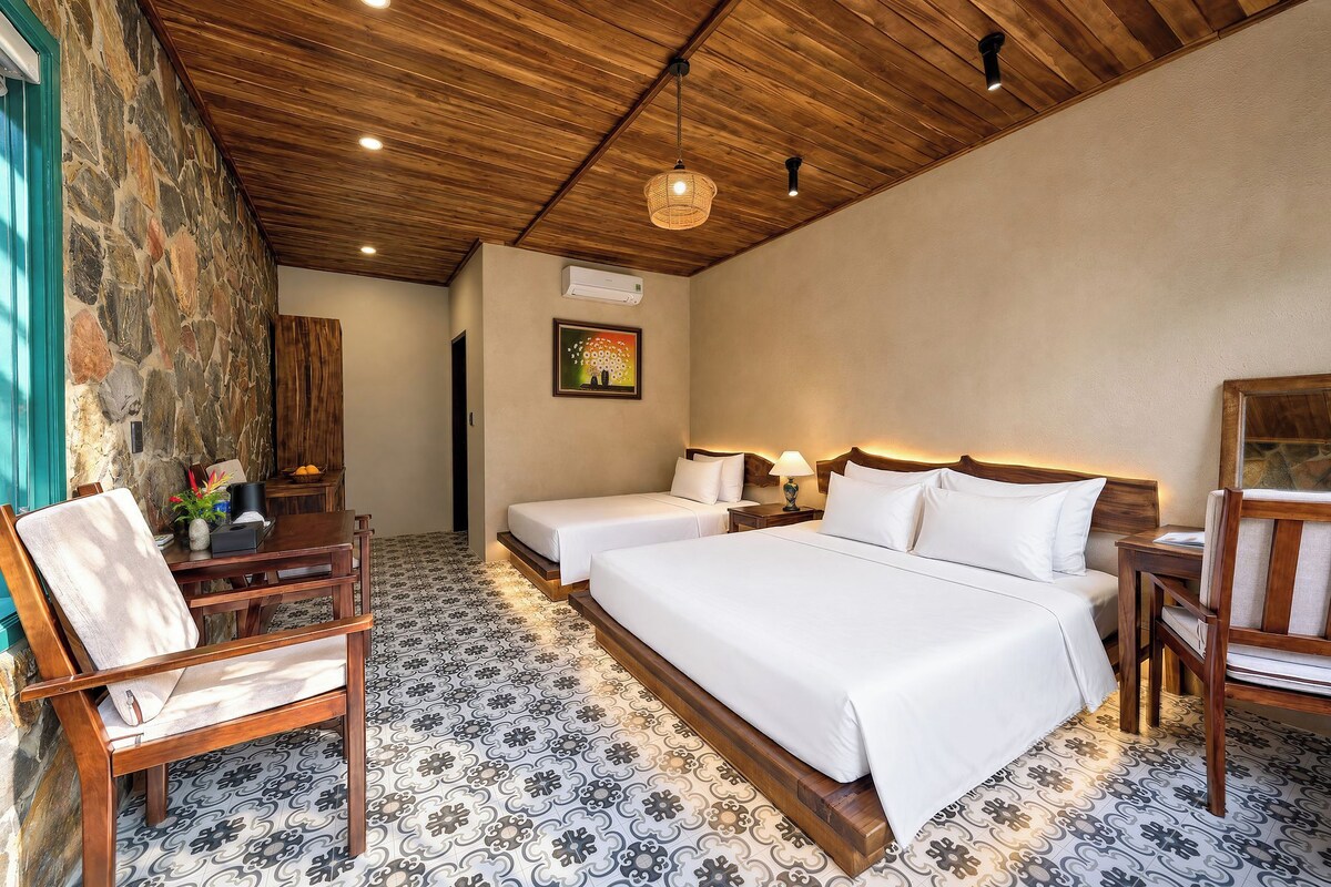 A hotel room with a wooden ceiling, two beds, a sitting area with chairs, and a patterned floor.