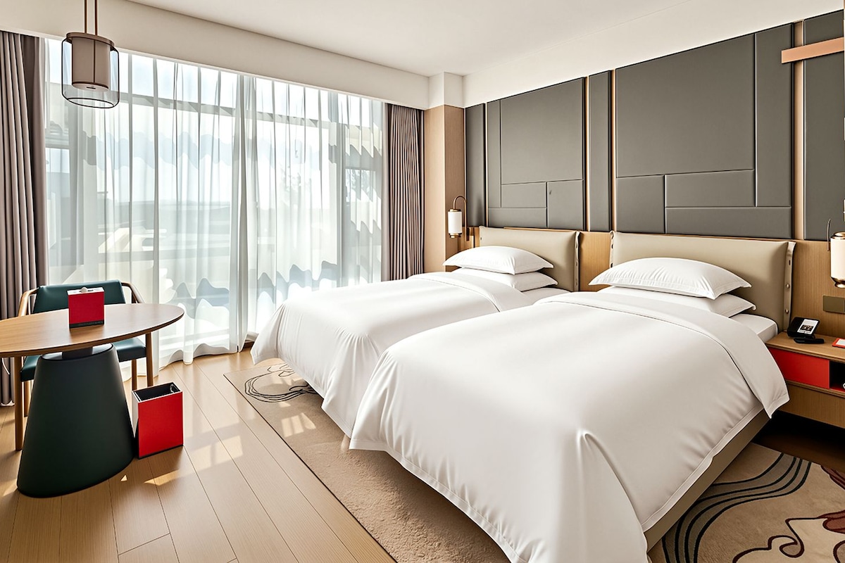 A hotel room with two beds, a dining table, and a view of the city.