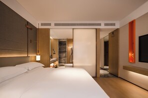 A hotel room with a large bed, a bathroom with a marble wall, and a TV mounted on the wall.