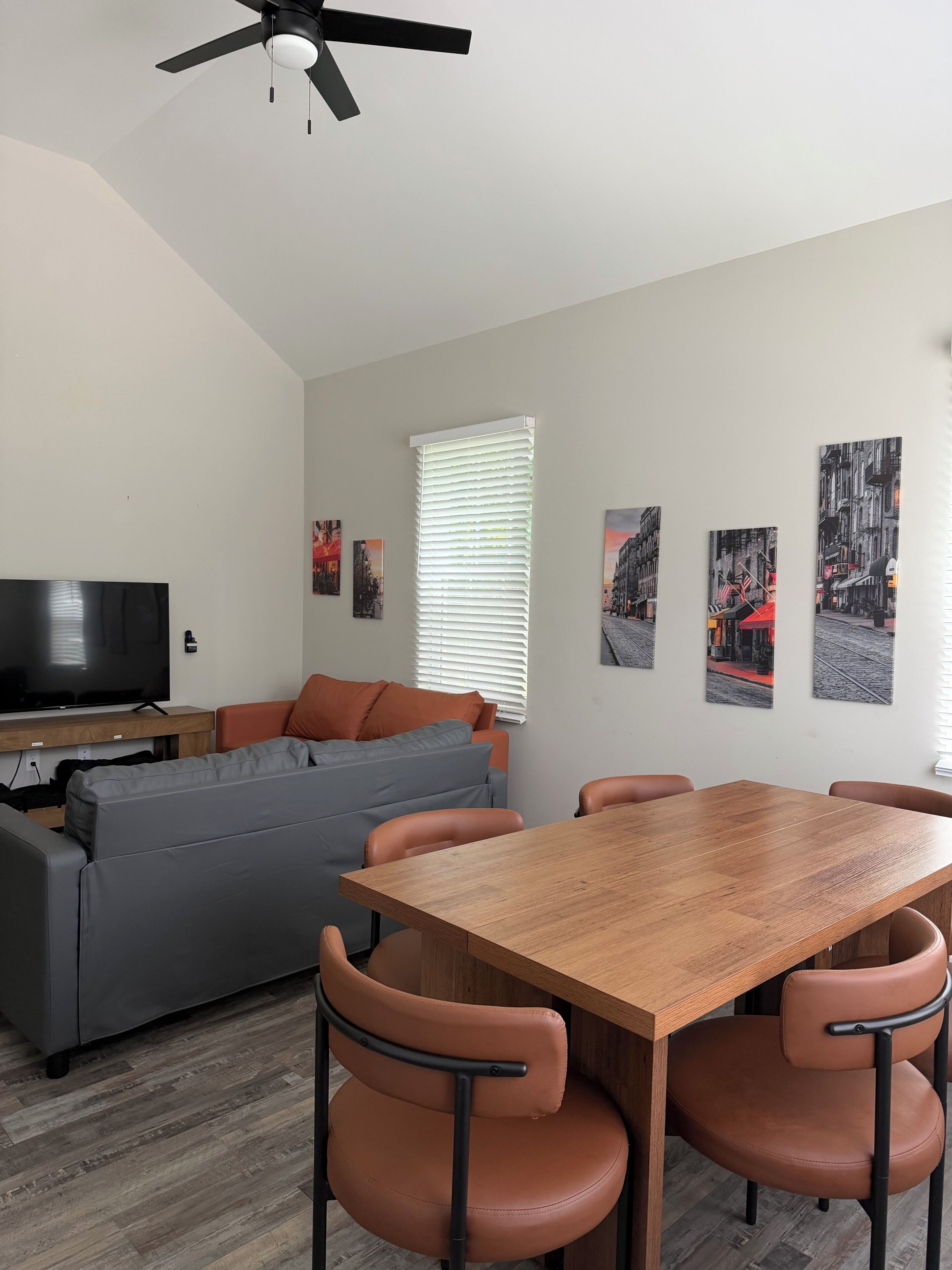 A modern living room with a grey sofa, a wooden dining table, and a ceiling fan.