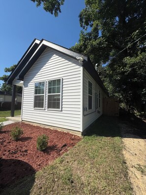 A single-story house with a gable roof, a front porch, and a small front yard with mulch and grass.