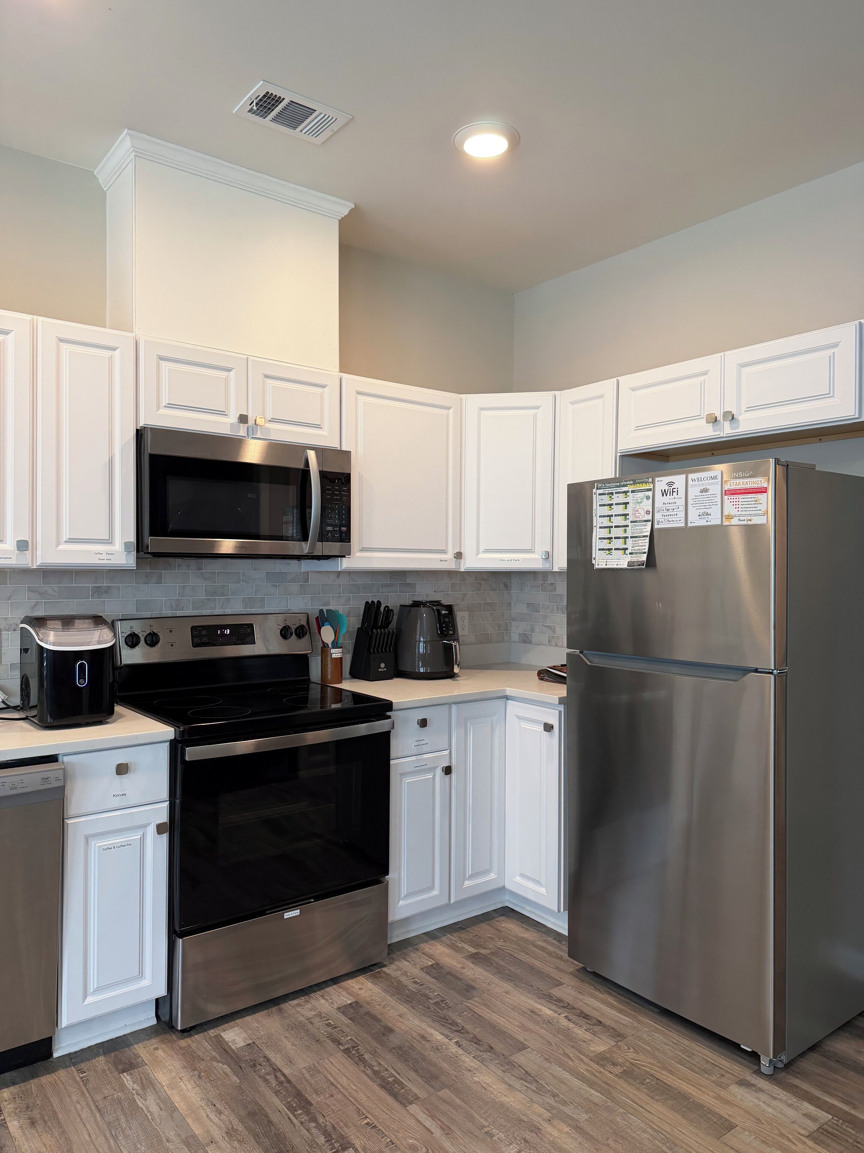 A modern kitchen with white cabinetry, stainless steel appliances, and a wood floor.