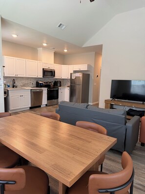 Una cocina moderna con gabinetes blancos, electrodomésticos de acero inoxidable y una zona de comedor con mesa de madera y sillas de cuero.