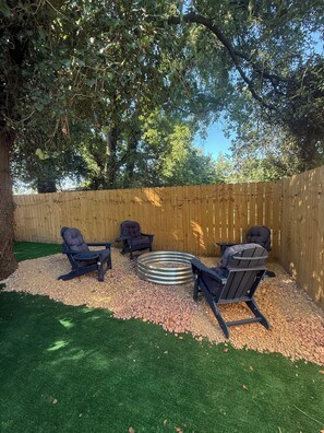 A backyard with a wooden fence, a circular fire pit, and two Adirondack chairs. - Close to downtown, HotTub, Fire Pit, Full Kitchen (Savannah)