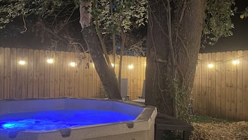 A hot tub with a blue light, surrounded by a wooden fence and trees.