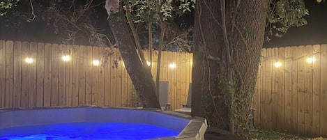 A hot tub with a blue light, surrounded by a wooden fence and trees.