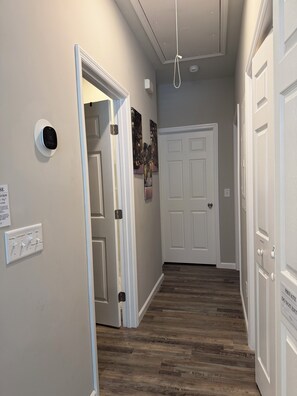 A hallway with a wooden floor, white walls, and a closed door at the end.