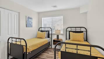 Une chambre avec deux lits, une table de chevet, une lampe, une fenêtre avec des stores et une porte.