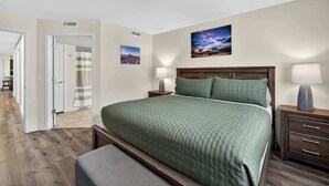 Une chambre à coucher comprenant un lit, des lampes de chevet, une table de chevet, une tête de lit en bois, une fenêtre et une porte donnant sur une autre pièce.