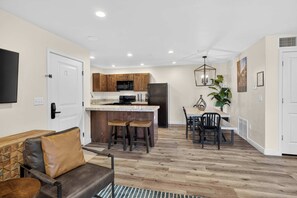A modern kitchen with wooden cabinets, a central island, and a dining area with a table and chairs. - 4-C Canyonlands Redcliff Condo (Pool View) (Moab)
