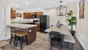 A kitchen with wooden cabinets, a granite countertop, a black refrigerator, and a dining area with a table and chairs. - 4-F Las Sal Mountain Condo (2nd Floor/Pool View) (Moab)