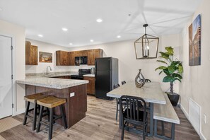 A kitchen with wooden cabinets, a granite countertop, a black refrigerator, and a dining area with a table and chairs. - 4-F Las Sal Mountain Condo (2nd Floor/Pool View) (Moab)
