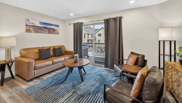 A living room with a sofa, coffee table, and chairs, a balcony with curtains, and a painting on the wall. - 4-F Las Sal Mountain Condo (2nd Floor/Pool View) (Moab)