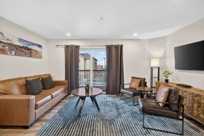 Ein modernes Wohnzimmer mit Sofa, Sessel, Couchtisch und Fernseher.