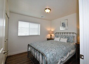 A bedroom with a metal bed frame, a bedside lamp, a window with blinds, and a ceiling light fixture. - 2-C Spanish Valley Condo (Moab)