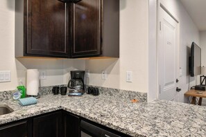 A kitchen with granite countertops, dark wood cabinets, a coffee maker, and a dishwasher. - 2-C Spanish Valley Condo (Moab)