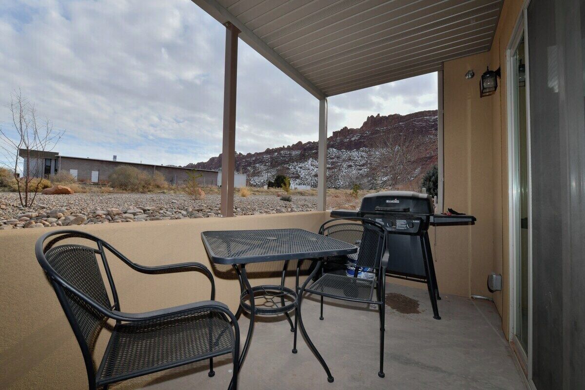 An outdoor patio with a table and chairs, a grill, and a view of a mountainous landscape.