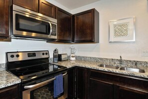 A kitchen with dark wood cabinets, a stainless steel microwave, a black stove, and a granite countertop. - 2-C Spanish Valley Condo (Moab)