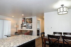 A modern kitchen with granite countertops, a dining area with wooden chairs, and a ceiling light fixture. - 2-C Spanish Valley Condo (Moab)
