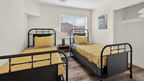 Quarto com duas camas, janela com persianas, luminária e um quadro na parede.