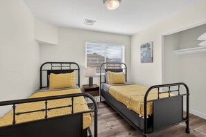 Ein Zimmer mit zwei Betten, einem Fenster mit Jalousien, einer Lampe und einem Bild an der Wand.