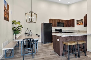 Una cocina moderna con armarios de madera, un refrigerador negro, una encimera de granito y un comedor con un banco y sillas.