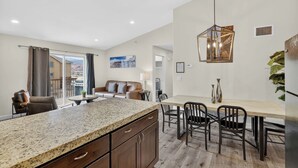 Uma cozinha moderna com bancadas de granito, uma sala de jantar com mesa e cadeiras de madeira e uma sala de estar com sofá e vista para o exterior.