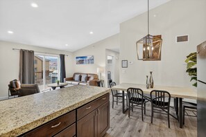 Eine moderne Küche mit Granit-Arbeitsplatten, ein Essbereich mit Holztisch und -stühlen sowie ein Wohnzimmer mit Sofa und Blick ins Freie.