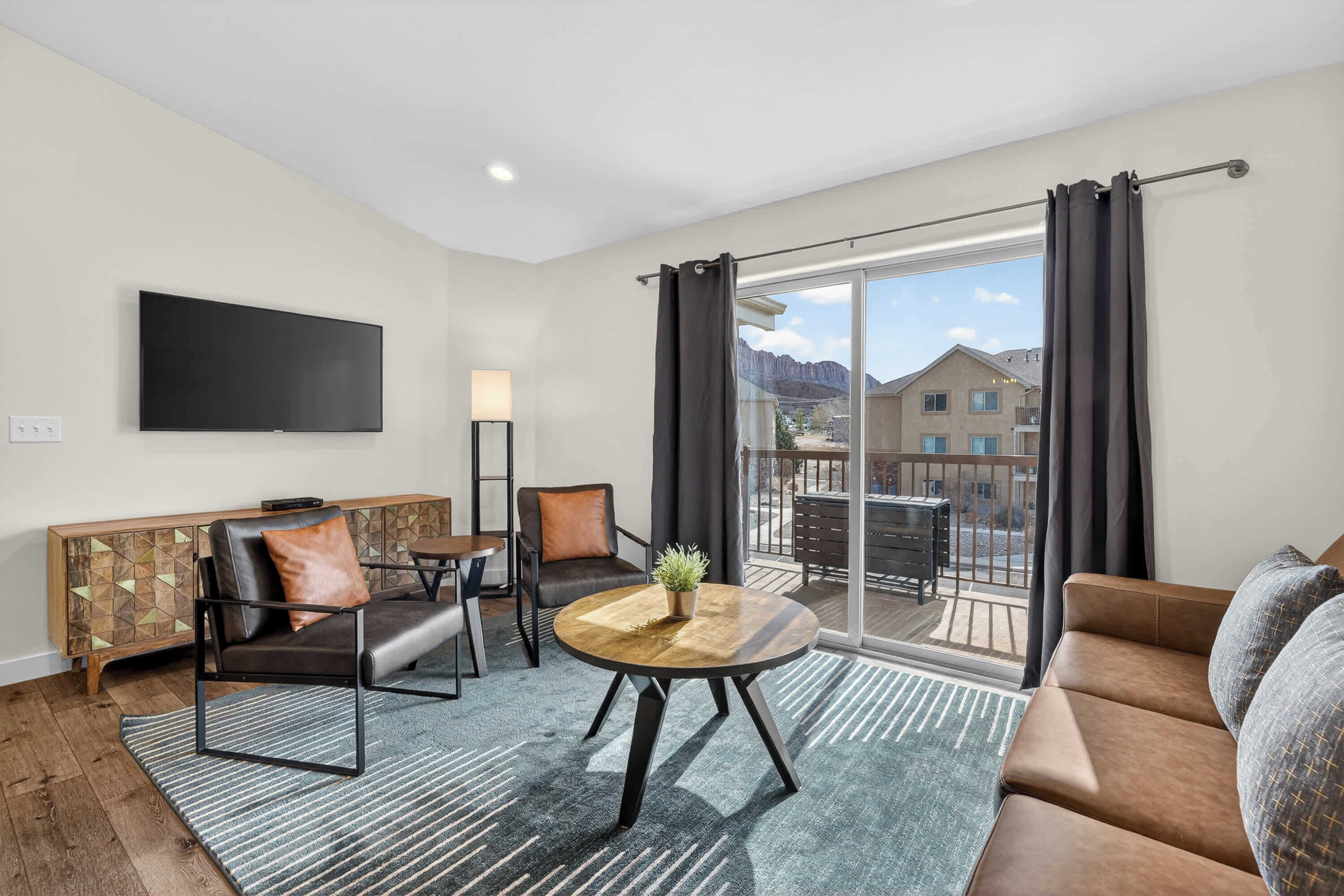 A modern living room with a flat-screen TV, a sofa, a coffee table, and a balcony with a view of buildings.