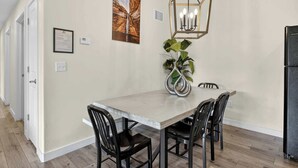 Uma sala de jantar com uma mesa, cadeiras, uma luminária pendente, uma planta e uma geladeira.