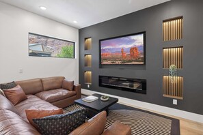Ein modernes Wohnzimmer mit einer Ledersofa, einem Flachbildfernseher an der Wand und dekorativer Wandbeleuchtung.