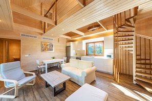 Ein modernes Interieur mit Holzbalkendecke, einer Couch, einem Esstisch und einer Treppe.