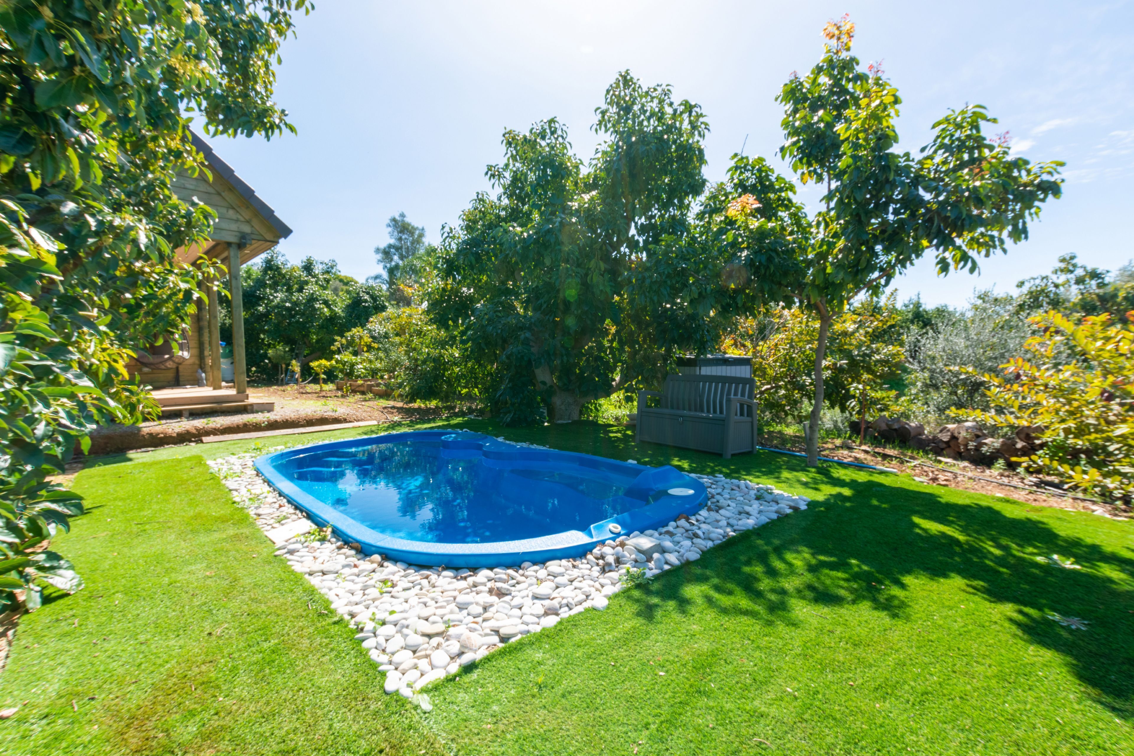 Un jardin à l’arrière de la maison avec une piscine entourée de galets blancs, de gazon verdoyant et d’arbres.