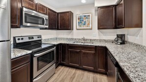A kitchen with dark wood cabinets, stainless steel appliances, a granite countertop, and a coffee maker. - 2-F Castle Valley Redcliff Condo (Moab)
