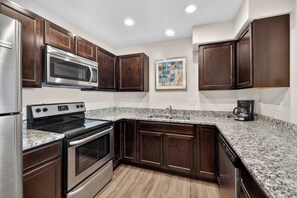 A kitchen with dark wood cabinets, stainless steel appliances, a granite countertop, and a coffee maker. - 2-F Castle Valley Redcliff Condo (Moab)