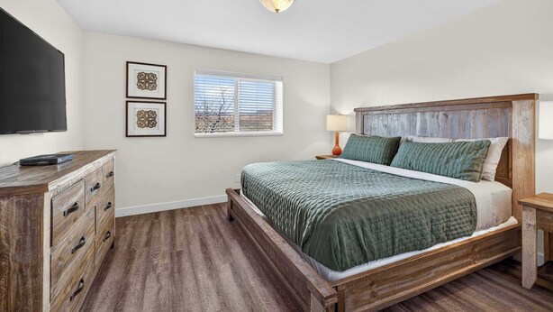 A bedroom with a bed, a dresser, a TV, and a window with blinds. - 2-F Castle Valley Redcliff Condo (Moab)