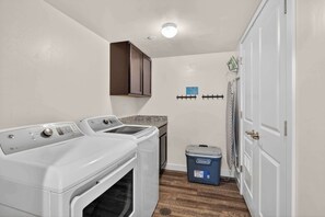 A laundry area with two washing machines, a dryer, a blue storage bin, and a door with a towel rack. - 2-F Castle Valley Redcliff Condo (Moab)