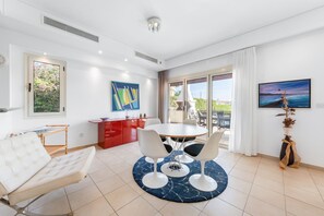 En moderne stue med sofa, spisebord med stole, et rødt skab og et billede på væggen.