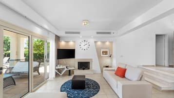 A modern living room with a large window, a flat-screen TV, a fireplace, and a sofa with a red pillow.