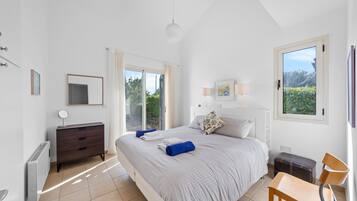A bedroom with a bed, a dresser, a chair, a desk, and a window with a view of greenery.