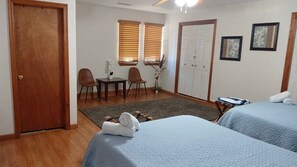 Habitación de hotel con dos camas, un escritorio, dos sillas, una mesita y una puerta.