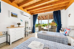 A bedroom with two beds, a dresser, a desk, and a balcony with a view.