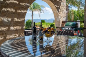 Une table en verre avec une bouteille de vin, un pichet et un saladier rempli de fruits.