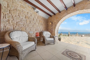 Ein Zimmer mit Stehwänden, Korbmöbeln, Fliesenboden und Blick aufs Meer.