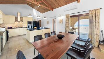 A modern kitchen with wooden beams, a dining area with a wooden table, and a view of the sea through a glass door.