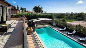 Ein Swimmingpool mit klarem, blauem Wasser, umgeben von einer Terrassenfläche mit Liegestühlen und einem überdachten Sitzbereich.