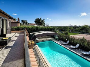 Una piscina con acqua cristallina circondata da un patio con lettini e una zona salotto coperta.